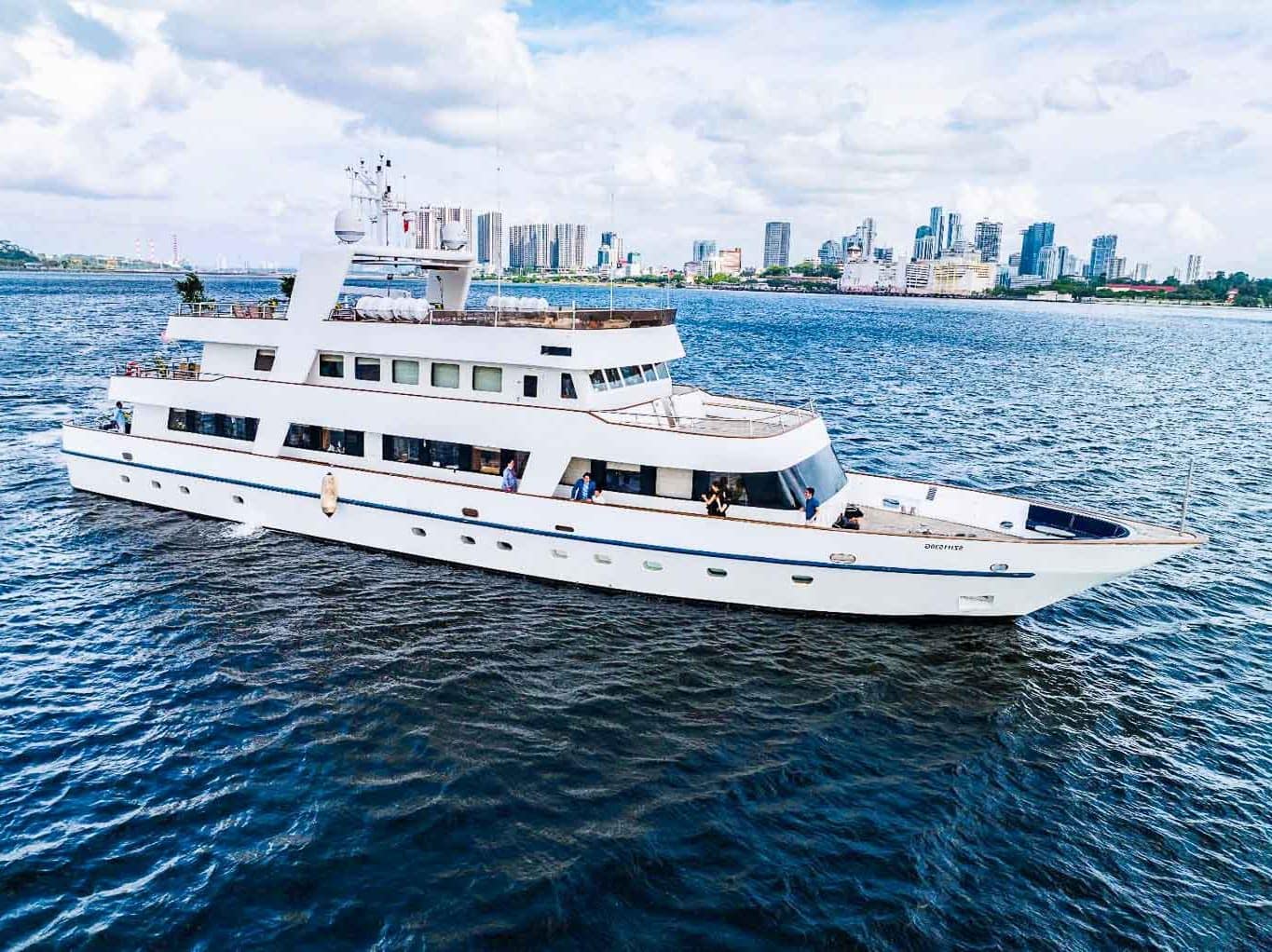 Star of the Sea classic white motor yacht with guests on deck cruising past Singapore city skyline
