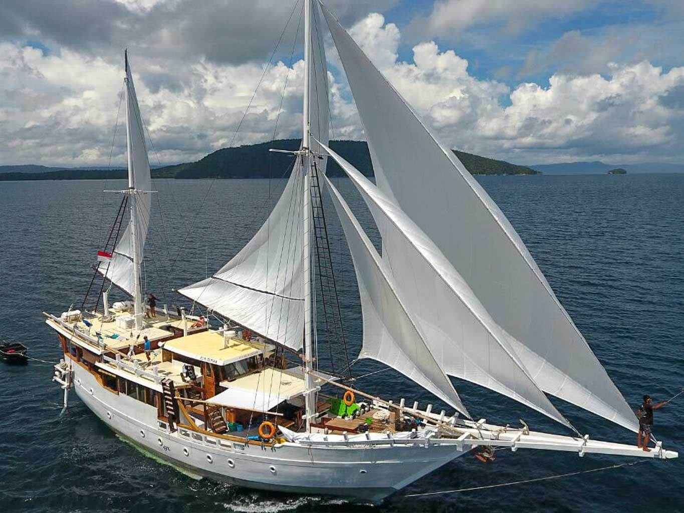 Teman Indonesian pinisi sailing yacht under full white sails with Indonesian flag flying and green tropical islands in background