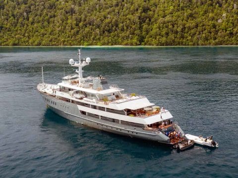 Aqua Blu luxury expedition motor superyacht anchored in calm tropical Indonesian waters surrounded by dense lush rainforest and island hills