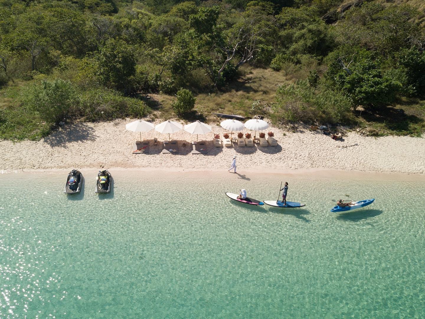 Aerial view of a secluded beach with SUP boards, kayaks, jet skis and sun loungers in Raja Ampat