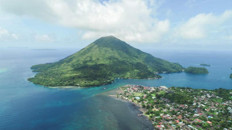 Aerial view of Gunung Banda Api volcano with traditional village in the foreground